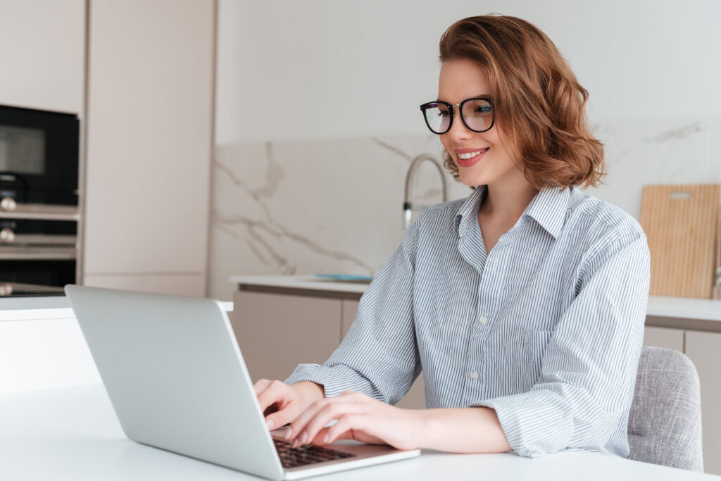 Femme élégante souriante, portant des lunettes et une chemise rayée, utilisant un ordinateur portable.