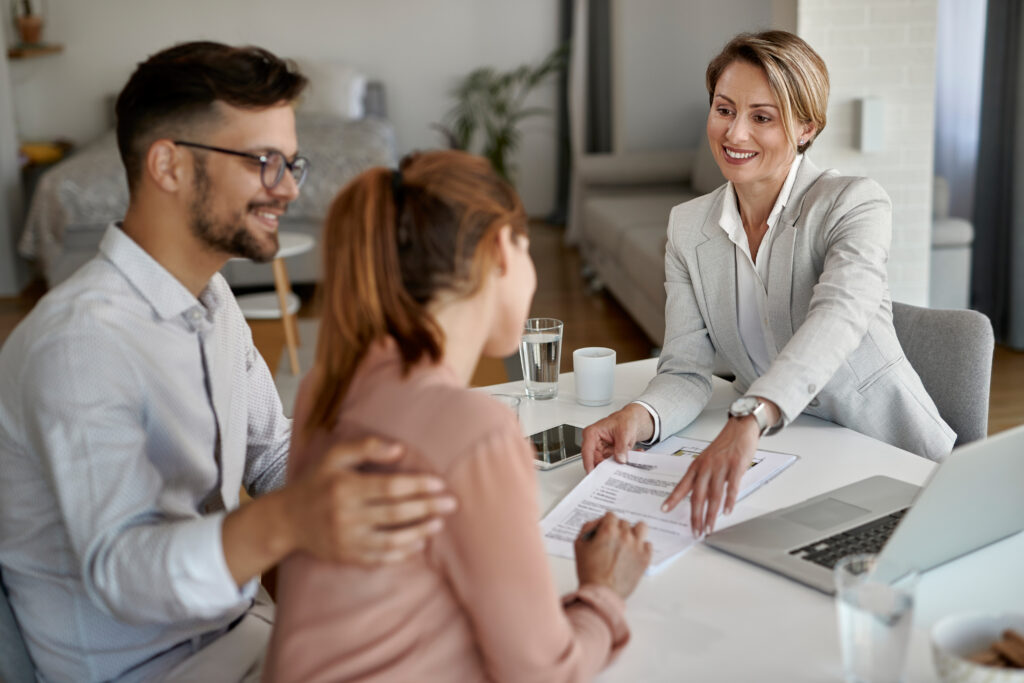 Agent immobilier souriant en rendez-vous avec un jeune couple, montrant l’emplacement de signature sur leur contrat.