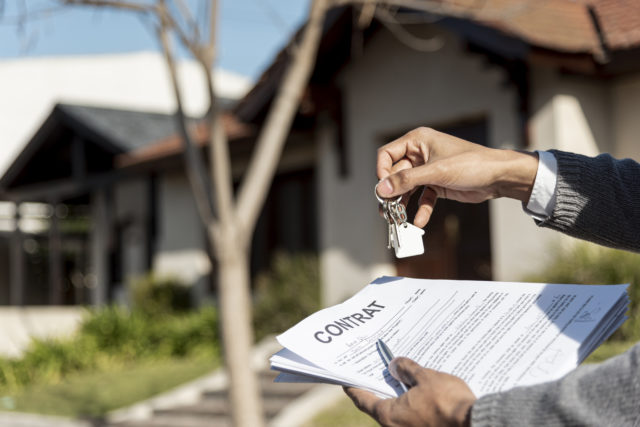 un homme tient un contrat de vente à réméré dans sa main devant une maison