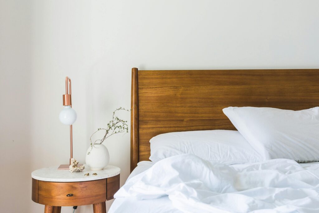 Chambre minimaliste avec linge de lit blanc, tête de lit en bois et lampe de chevet design.