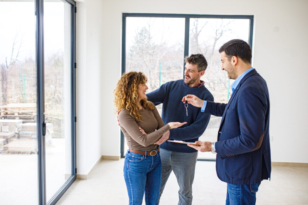 Agent immobilier remettant les clés d’une nouvelle maison à un jeune couple.